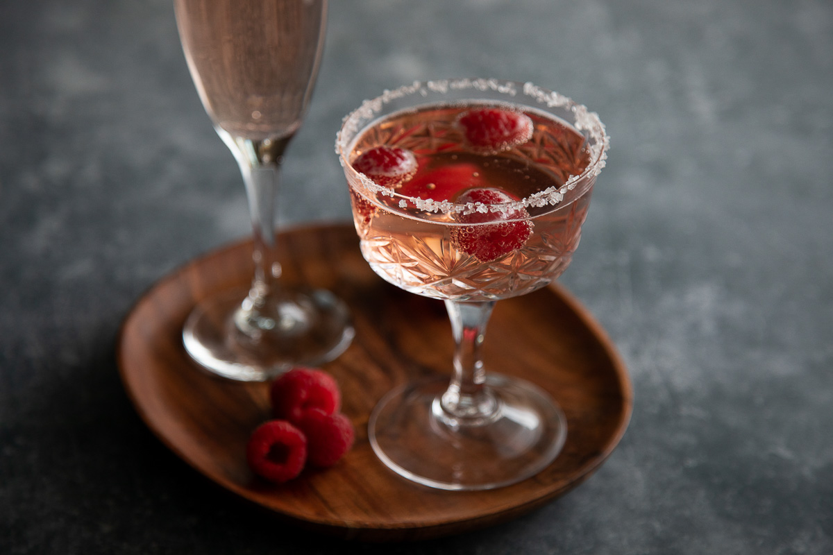 raspberry rosé cocktail in champagne coupe on brown plate