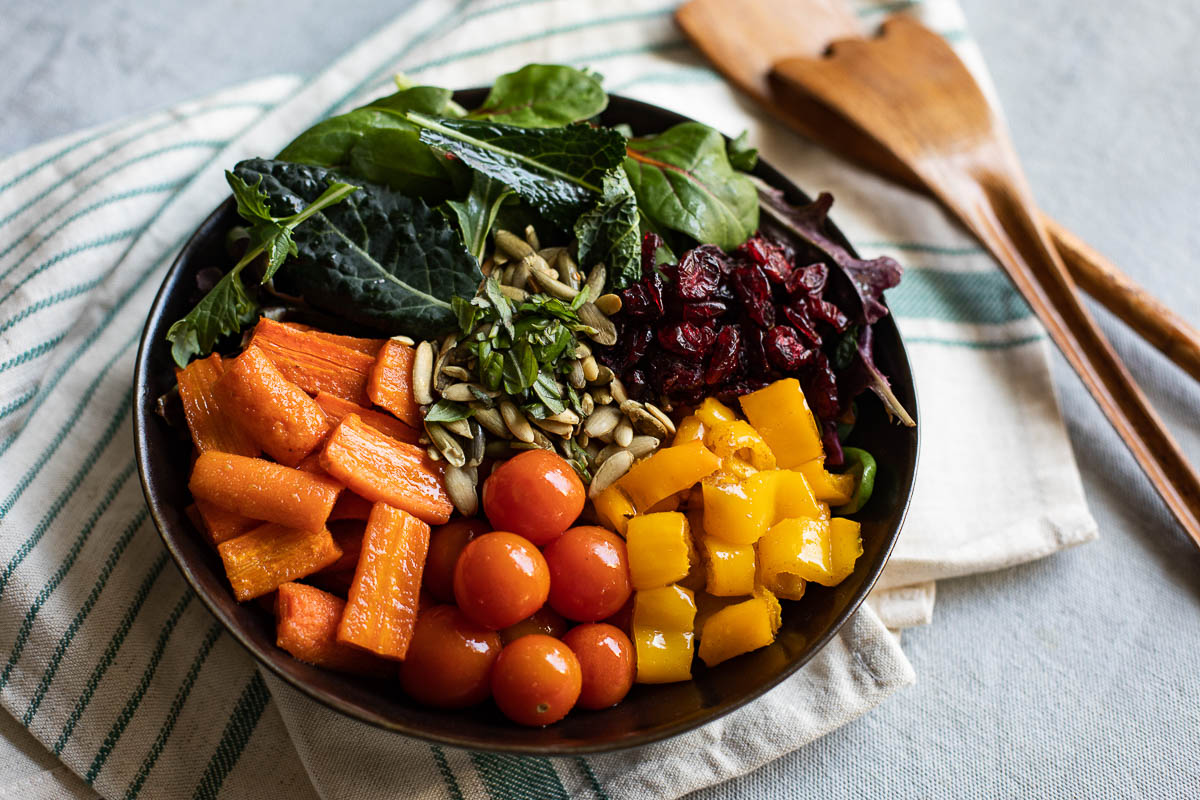 Summer Salad in Bowl with Roasted Carrots and bell peppers, cherry tomatoes, seeds and leafy greens