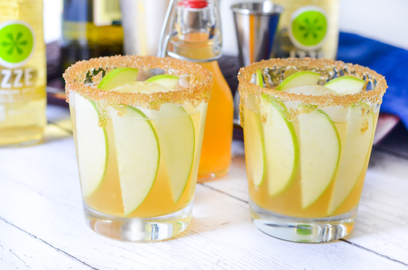 Two Glasses of Apple Whiskey cocktails on white wood panels.