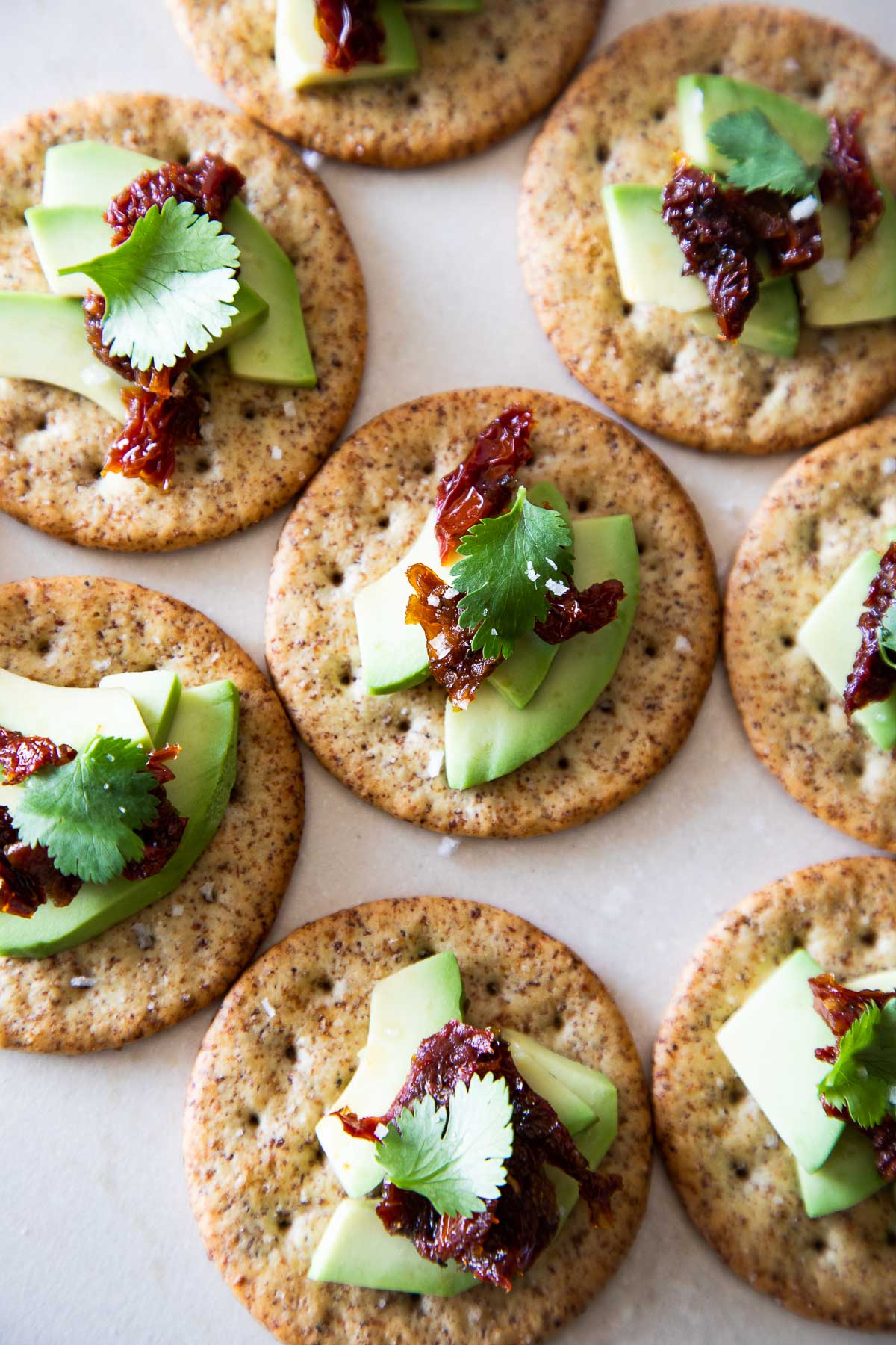 8 Avocado Topped Crackers with Sun Dried Tomato, touching on white background