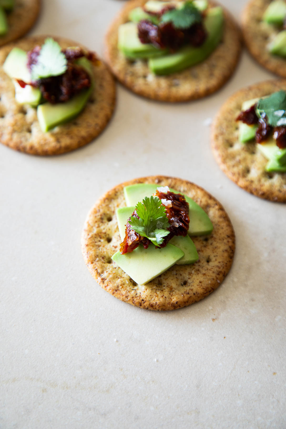 Avocado Crackers with Sun Dried Tomato. One in forefront, more blurred behind.