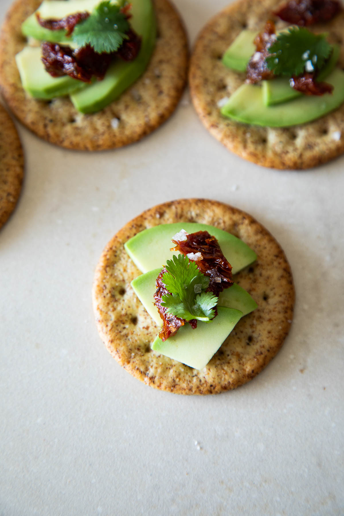 Avocado Crackers with Sun Dried Tomato, Cilantro Leaves, & Salt on Top
