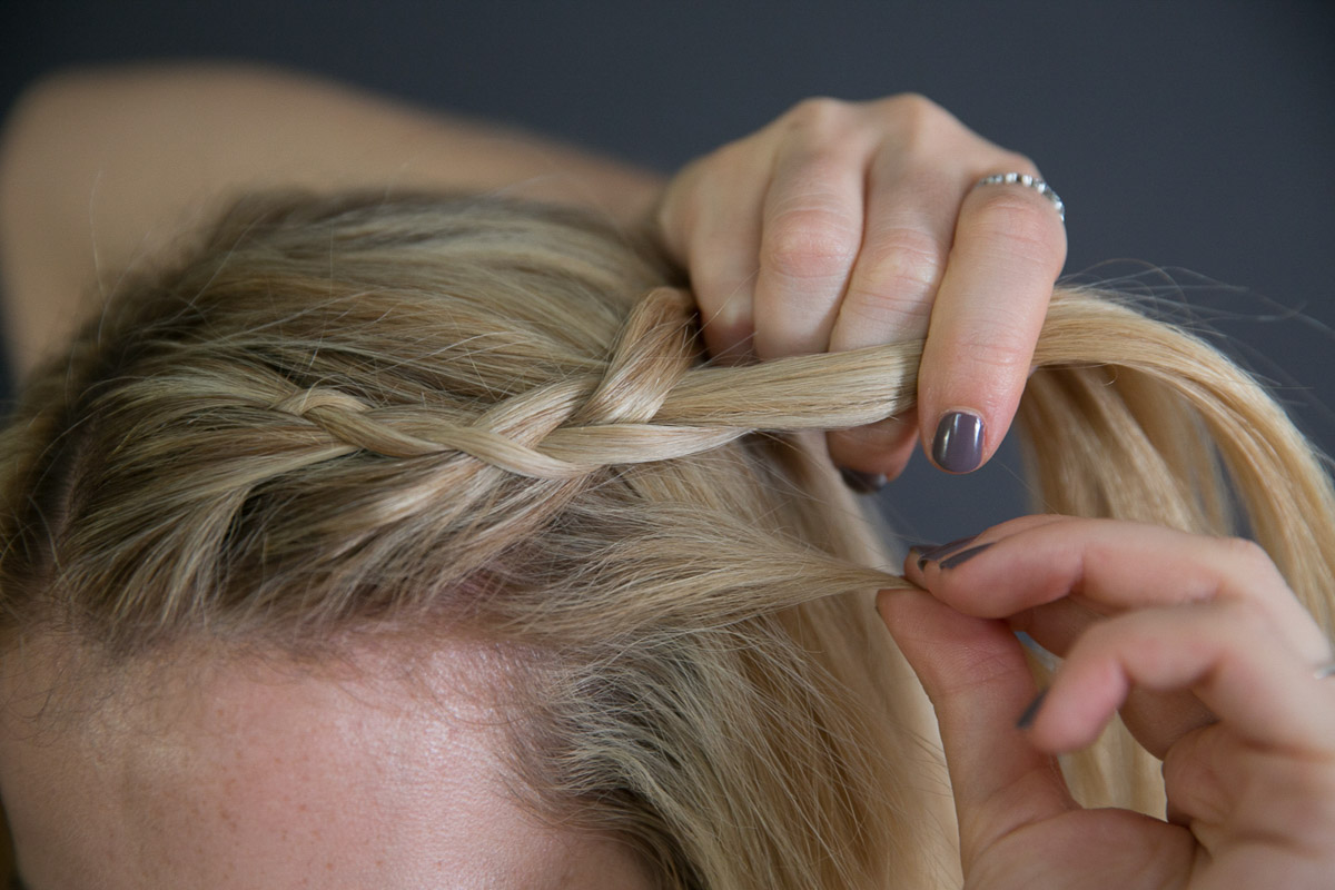 PUlling side braid back while braiding long blond hair.