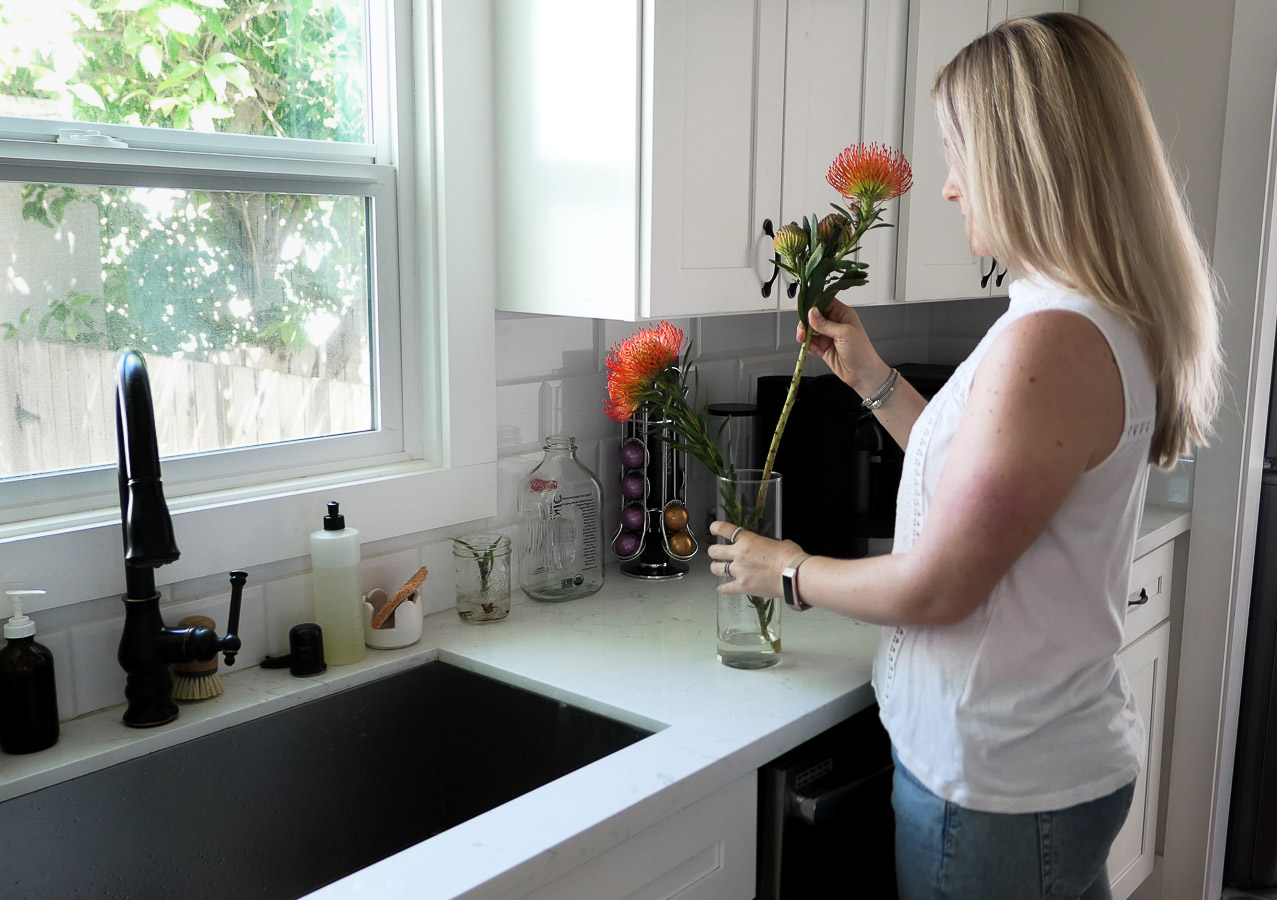 woman putting flower in vase by sink - sustainability guilt