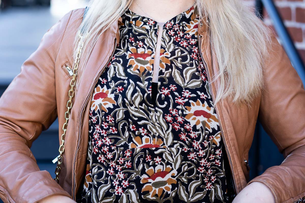 Close up of dark floral print top and open tan leather jacket