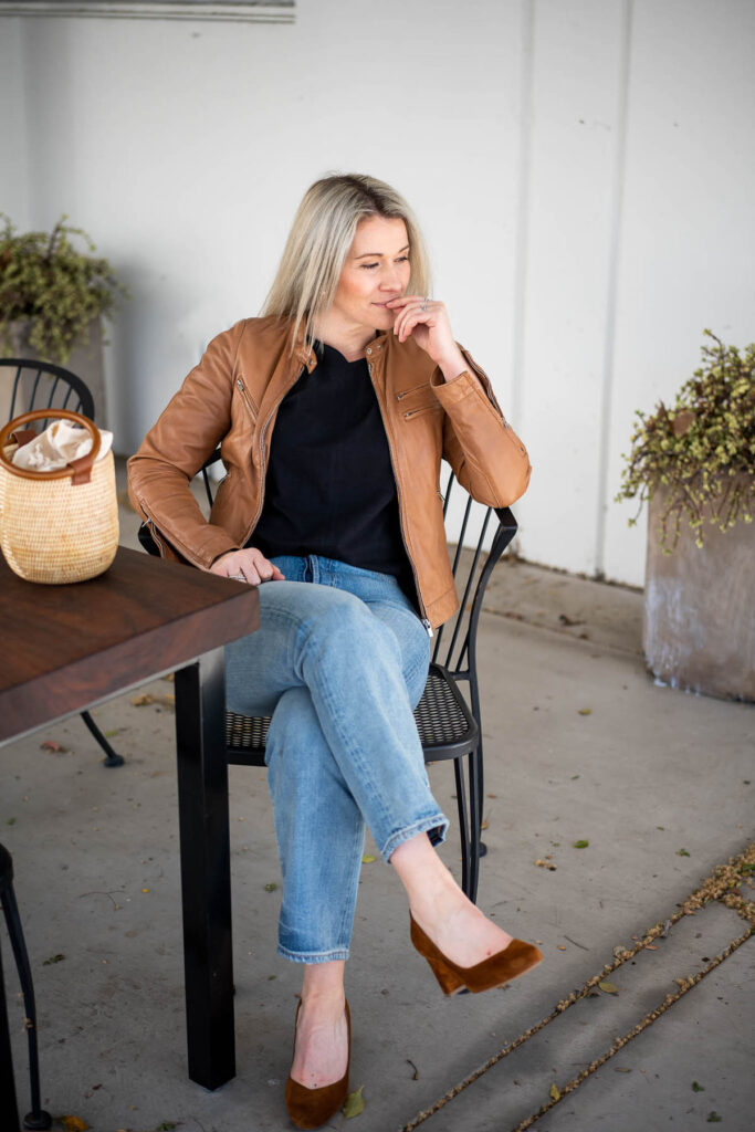 Luci Sitting in tan leather jacket, blue jeans,a nd sustainable suede pumps