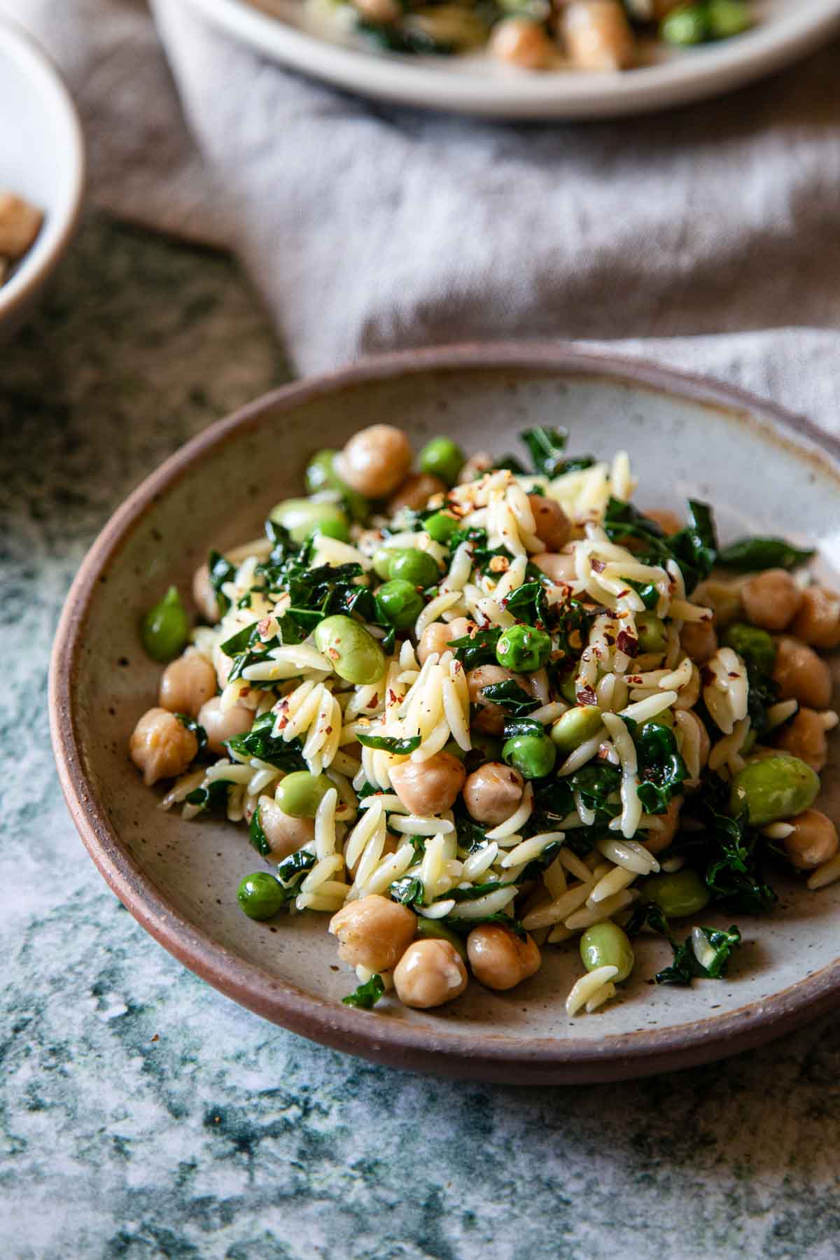 Orzo, pasta, spinach, and garbanzo beans on light pink plate - close up photo