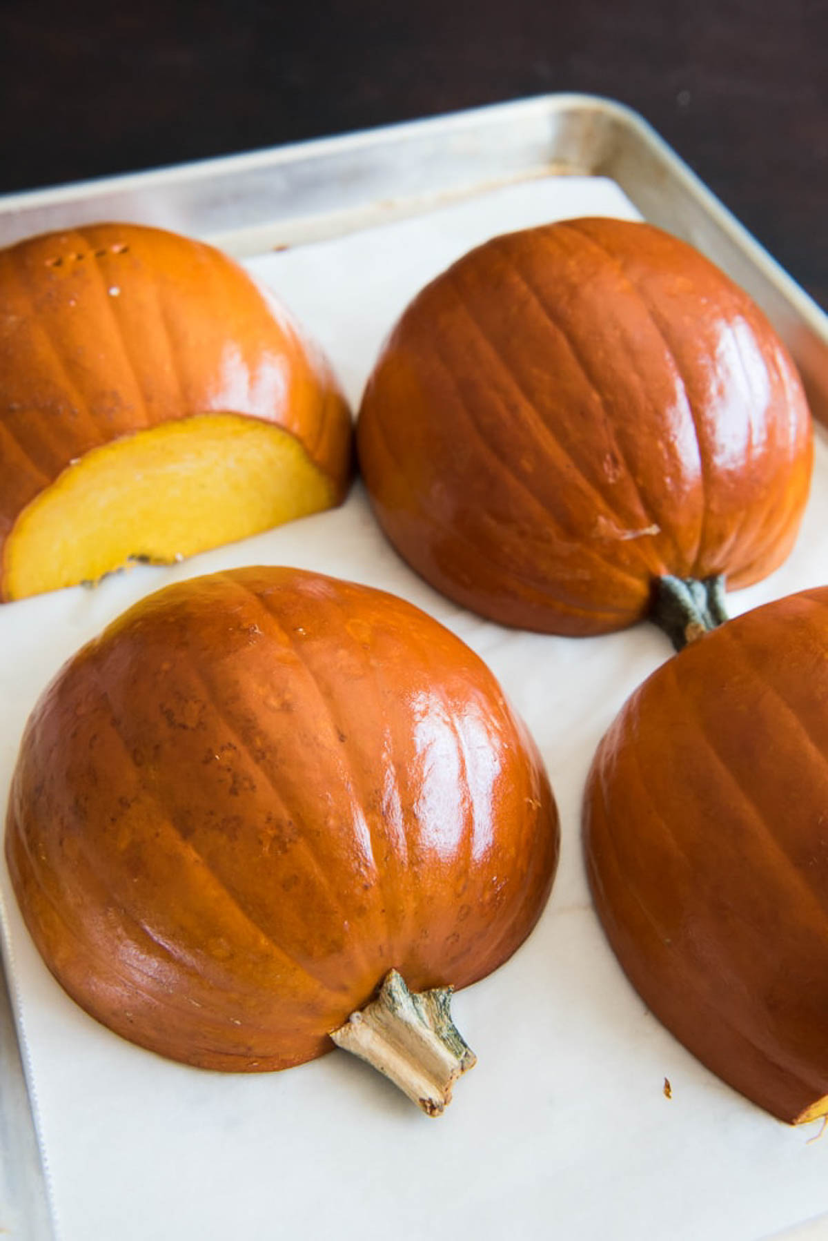 Pumpkin halves roasting cut-side down on a baking sheet