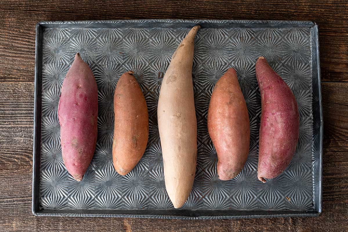Mixed whole raw sweet potatoes on baking pan - How to Store Sweet Potatoes