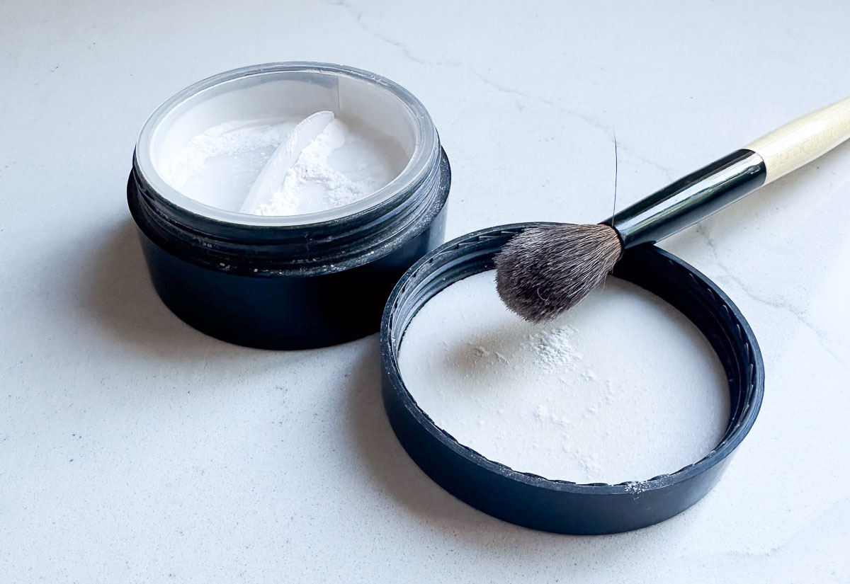 finishing powder container open on counter with powder brush - Best under eye concealer for mature skin 2