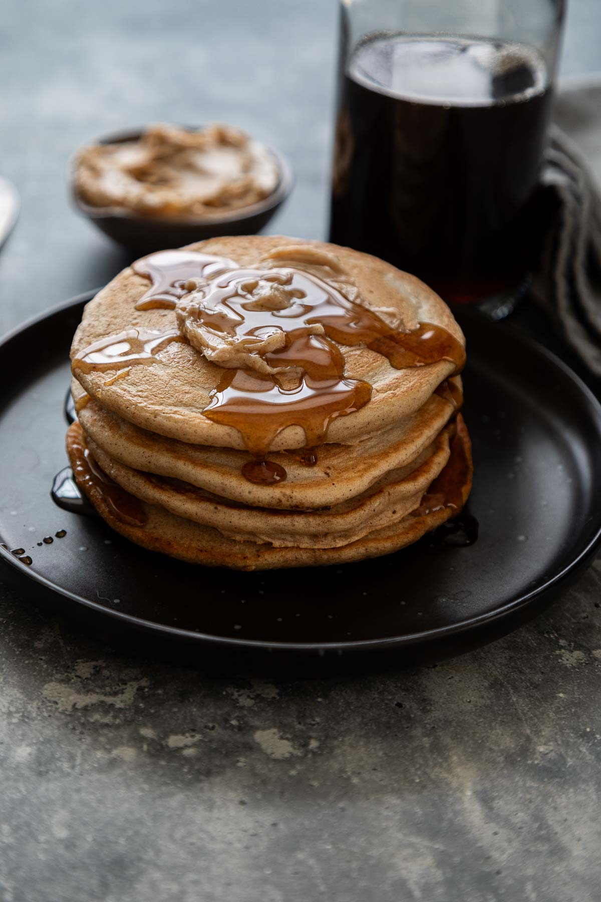 Cinnamon Pancakes stacked on black plate with syrup bottle in the background